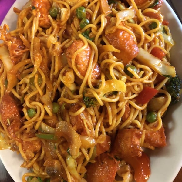 Close-up of Indian noodles with chicken, peas, and mixed vegetables in a savory sauce.