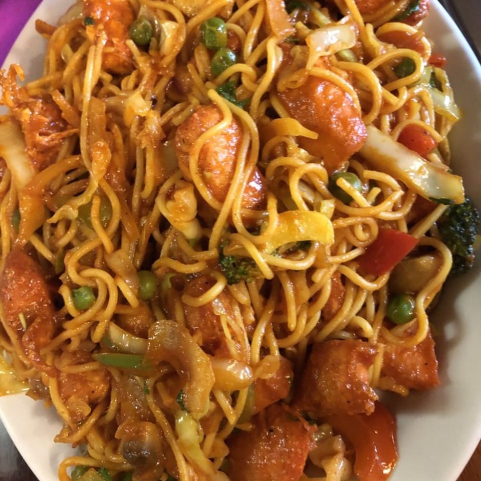 Close-up of Indian noodles with chicken, peas, and mixed vegetables in a savory sauce.
