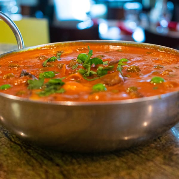 Close-up of a vibrant orange Indian curry with green herbs in a silver serving bowl.