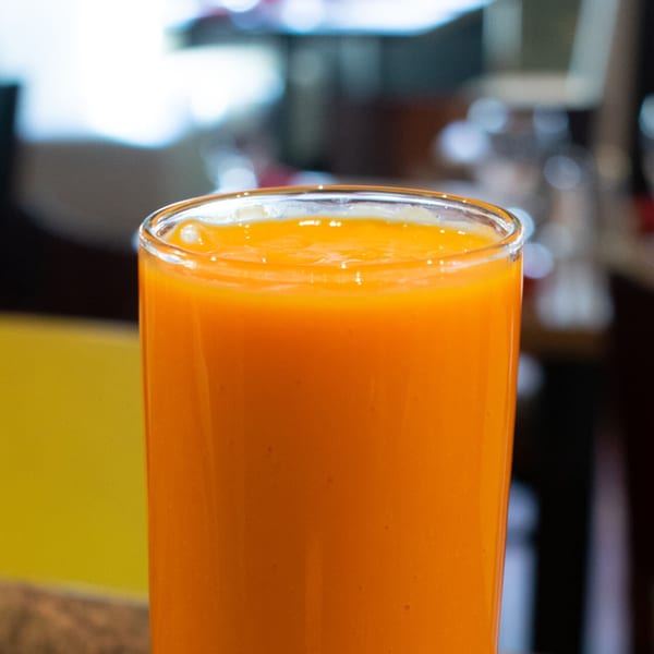 A vibrant orange mango lassi in a clear glass, a popular Indian drink.