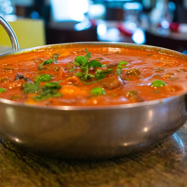 A vibrant red Indian curry, garnished with fresh herbs, served in a silver bowl.