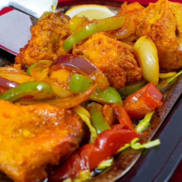 Indian chicken dish with bell peppers and onions, served on a sizzling platter with a lemon wedge.