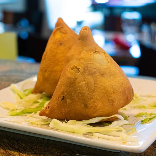 Two golden-brown Indian samosas, garnished with shredded lettuce, on a white rectangular plate.