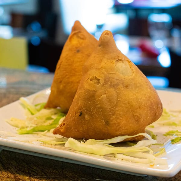 Two golden-brown samosas, a popular Indian appetizer, sit on a bed of shredded lettuce.