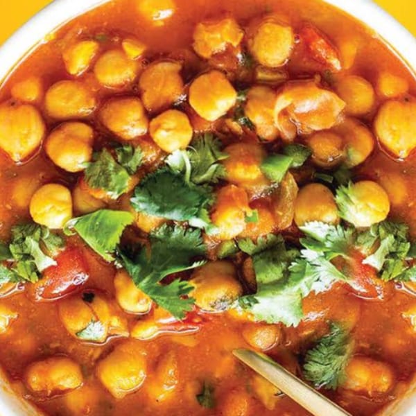 Close-up of Guras Spice House's Chana Masala, a chickpea curry with cilantro garnish and a spoon.
