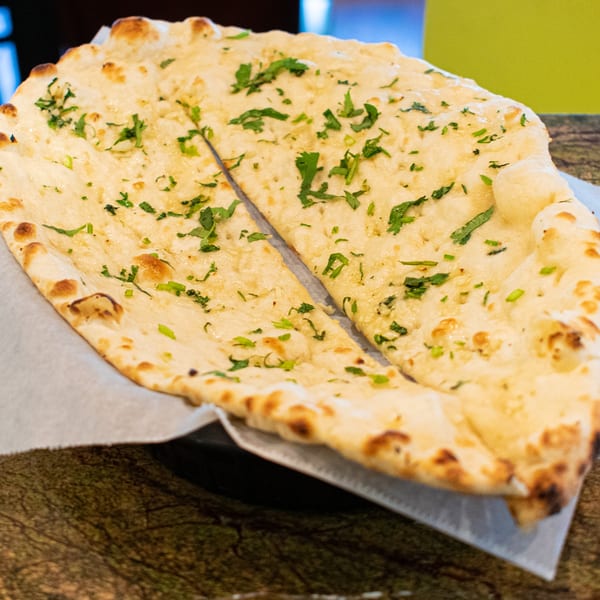Two pieces of golden-brown naan bread, sprinkled with fresh green herbs, served on a white paper liner.
