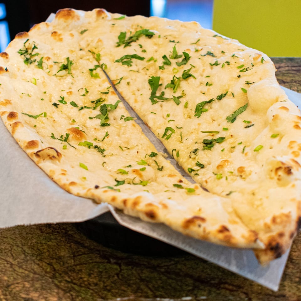 Two pieces of golden-brown naan bread, sprinkled with fresh green herbs, served on a white paper liner.